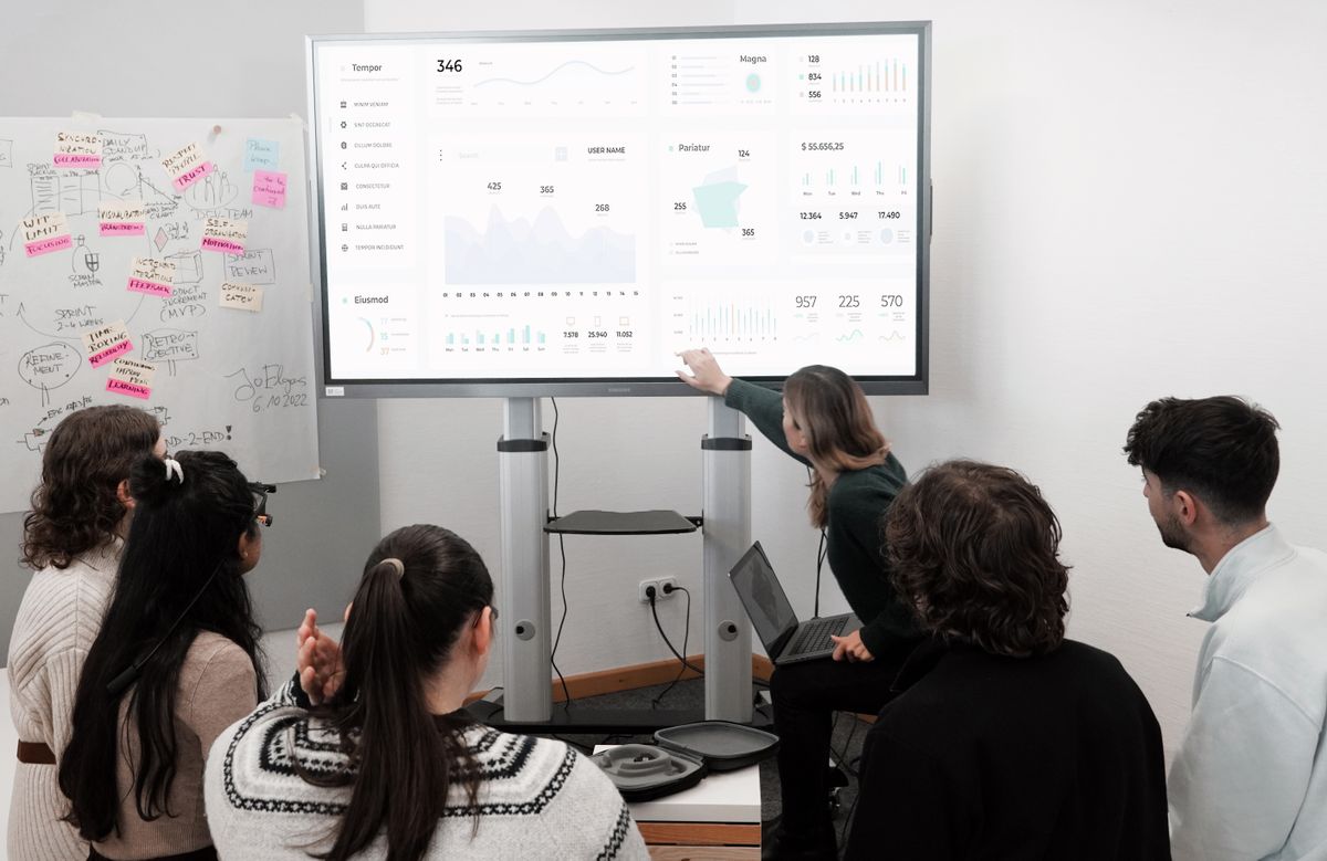 Team reviewing charts and a dashboard on a large presentation screen