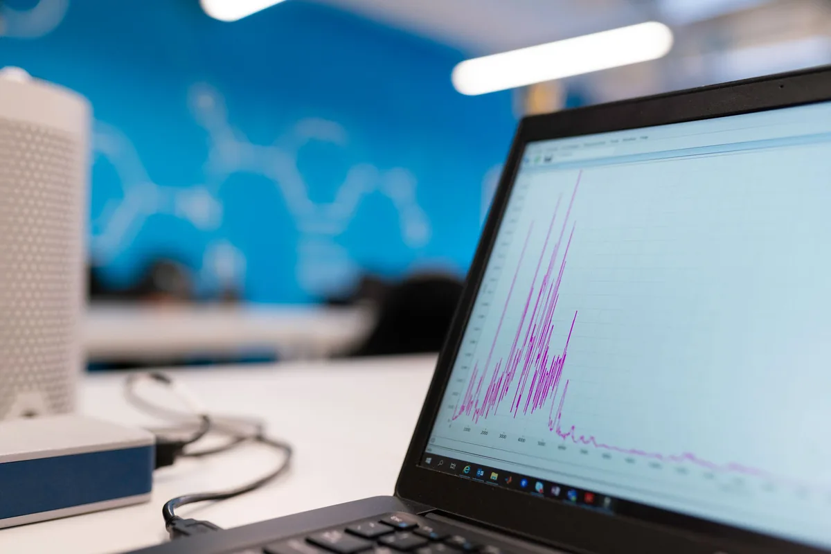 A laptop displaying a plotted measurement signal beside laboratory equipment.
