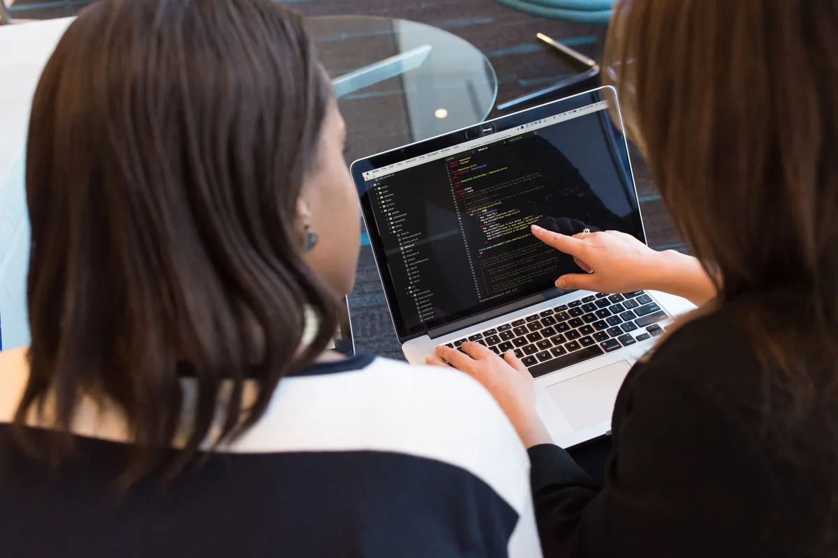 Two women reviewing programming code together on a laptop.