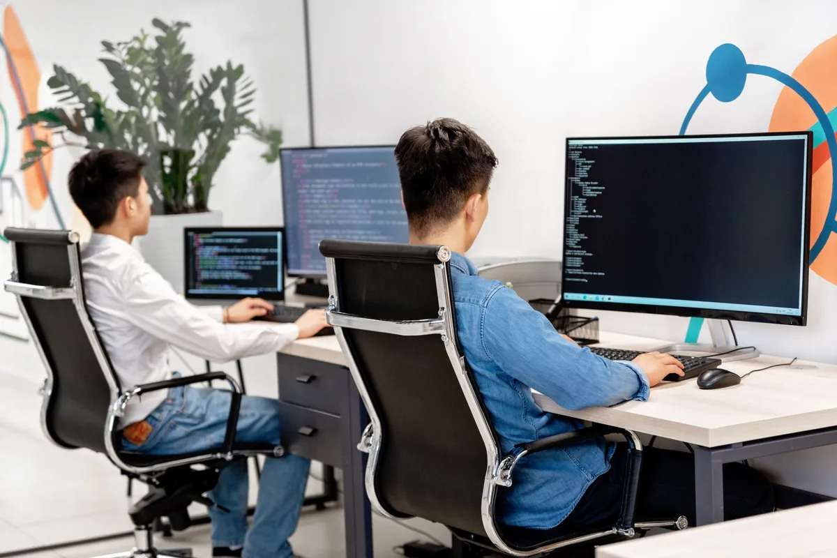 Two engineers working at computer monitors in a bright shared office.