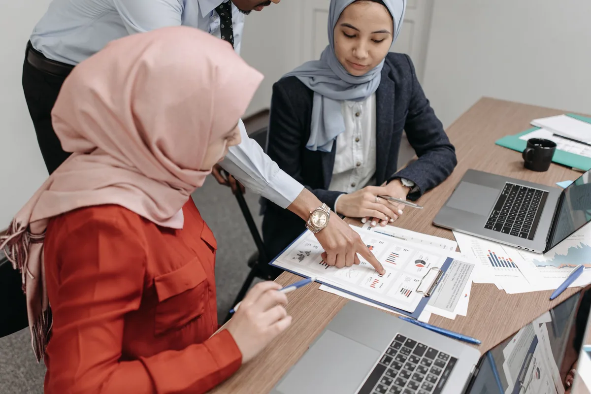 Three colleagues reviewing printed charts and documents at a shared office table.