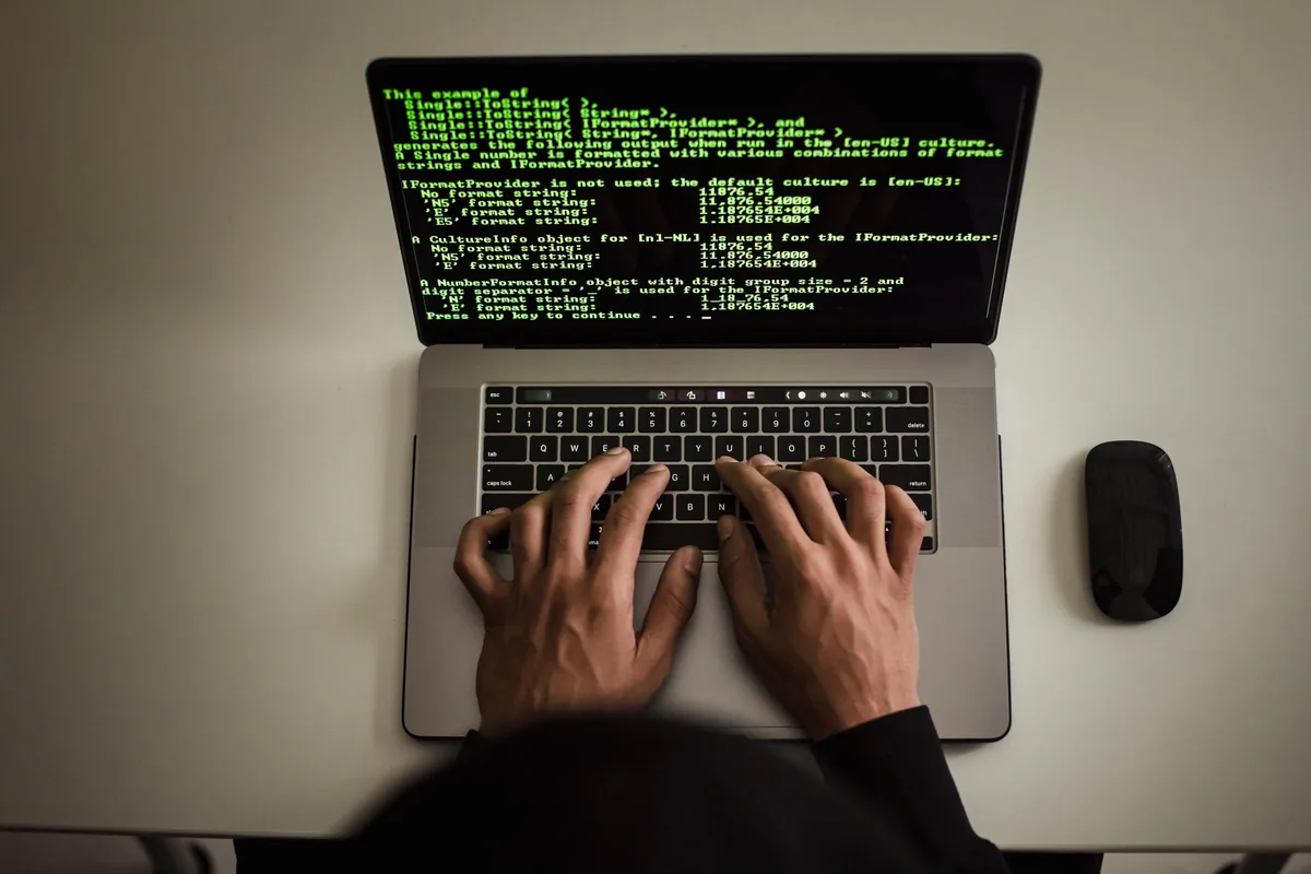 A developer typing on a laptop with programming code displayed on its screen.