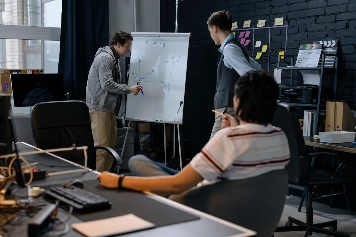 Colleagues discussing a process on a flipchart beside a work-in-progress board.