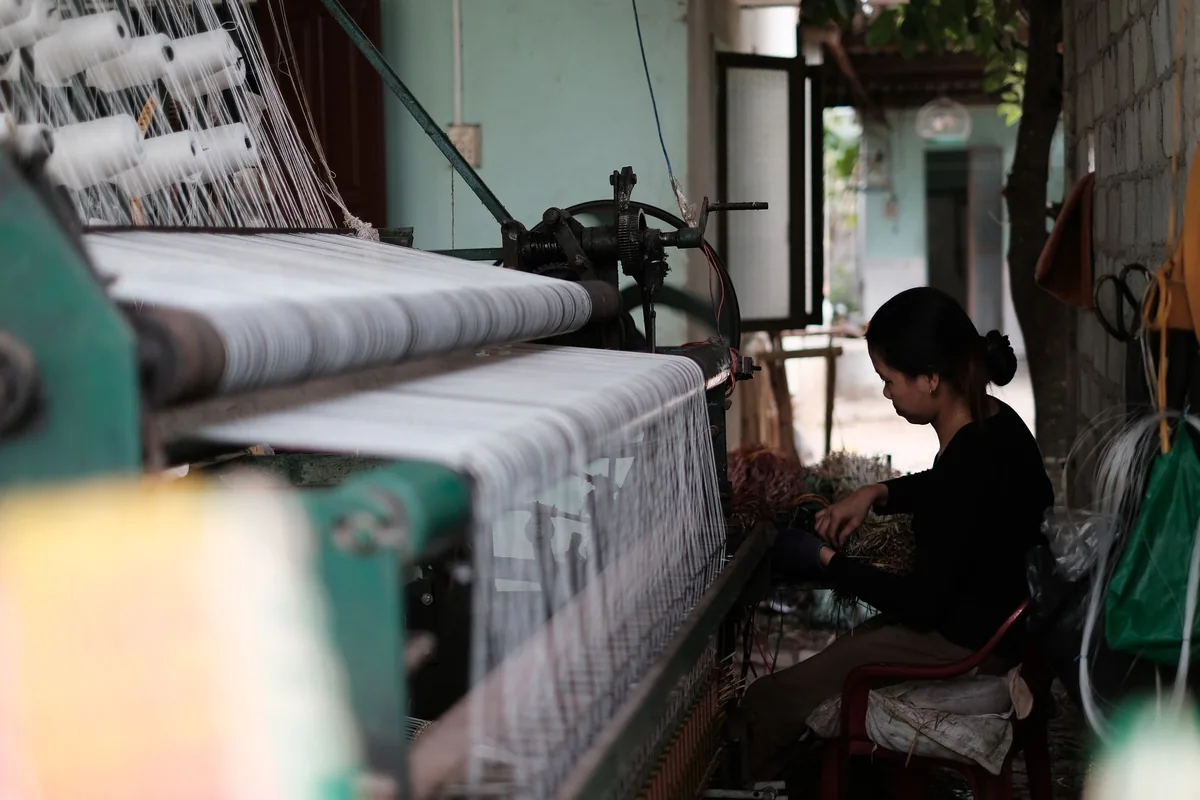 A textile worker operating a loom as fabric moves through the machine.